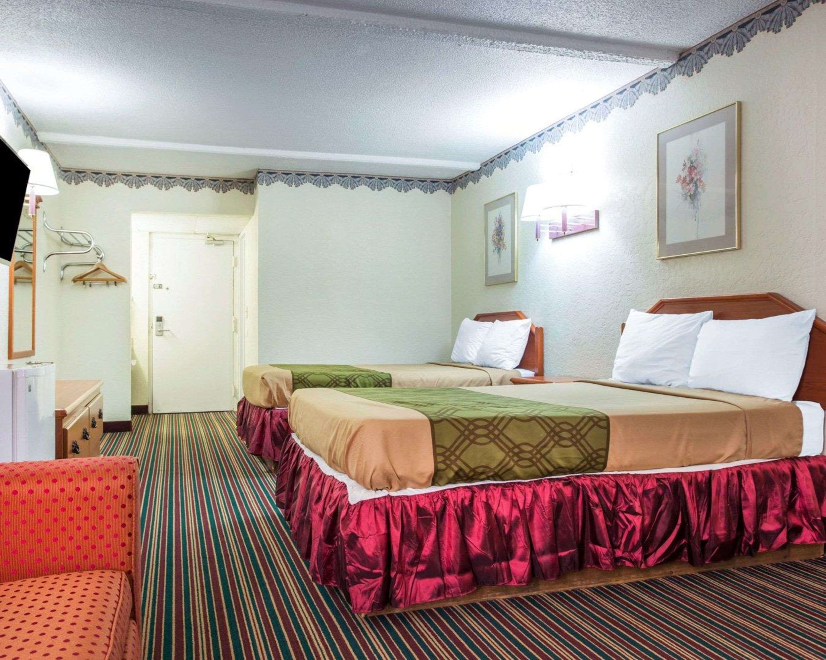 Una habitación de hotel con dos camas, una silla roja, un escritorio y una puerta.