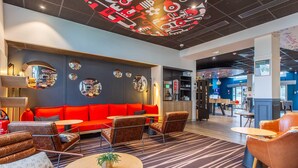 A modern lounge area with a red sofa, leather armchairs, and a round table with a plant. - B&B Hotel Orléans Centre Foch (Orléans)