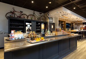 A breakfast bar with various food items, a bicycle mounted on the wall, and a wall with drawings. - B&B Hotel Orléans Centre Foch (Orléans)