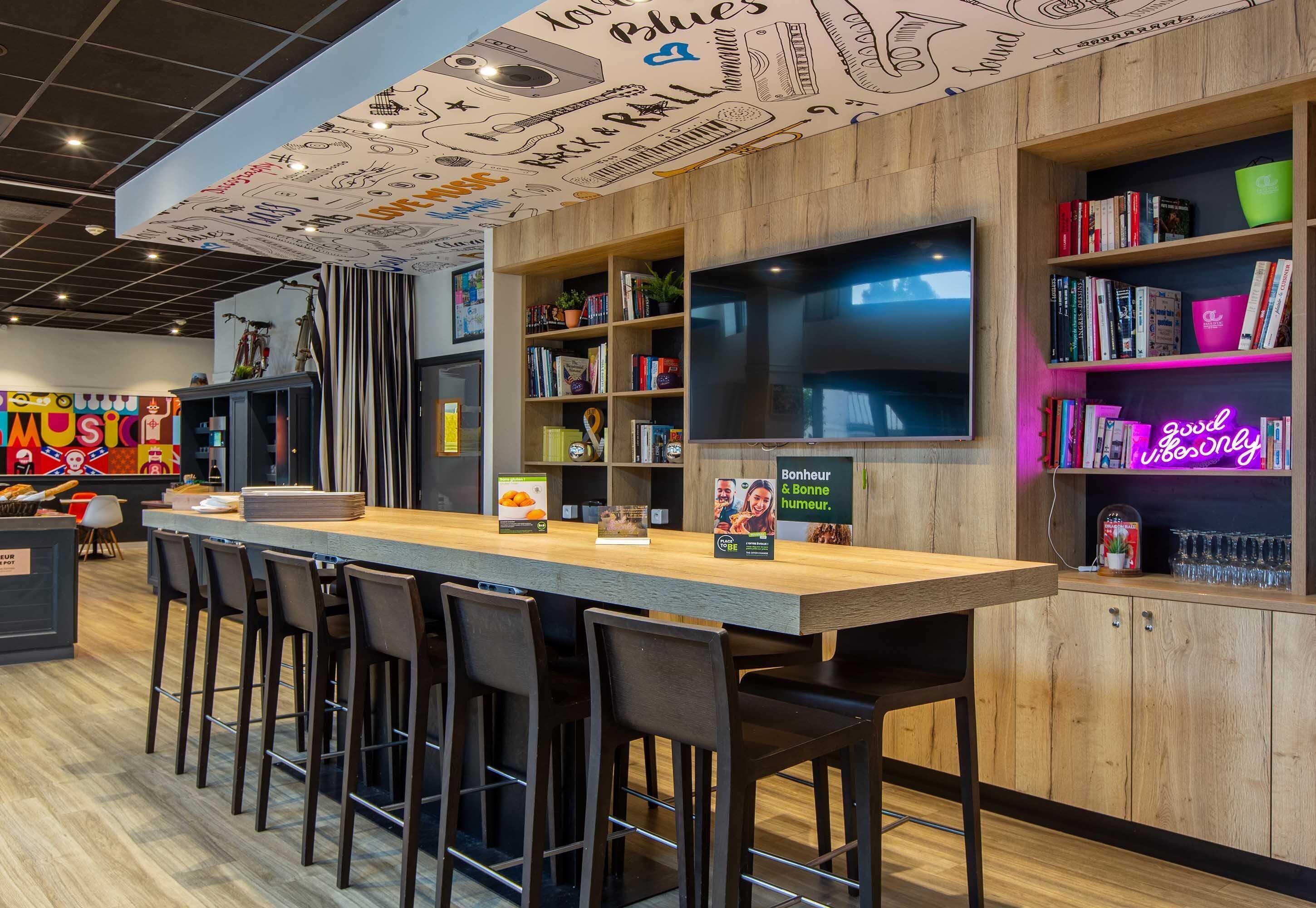 Una zona de bar con mostrador de madera, taburetes, estanterías y un letrero de neón.