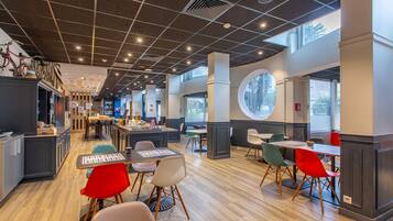 A modern restaurant with a high ceiling, wooden flooring, and a mix of red and white chairs.