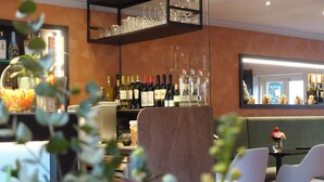 Zona bar con scaffali pieni di bottiglie e bicchieri, area salotto con sedie e uno specchio che riflette l'interno.