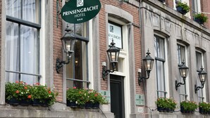 Segnaletica di un hotel con il nome "PRINSENGRACT HOTEL" e un logo verde. Sui davanzali, cassette con piante e fiori.