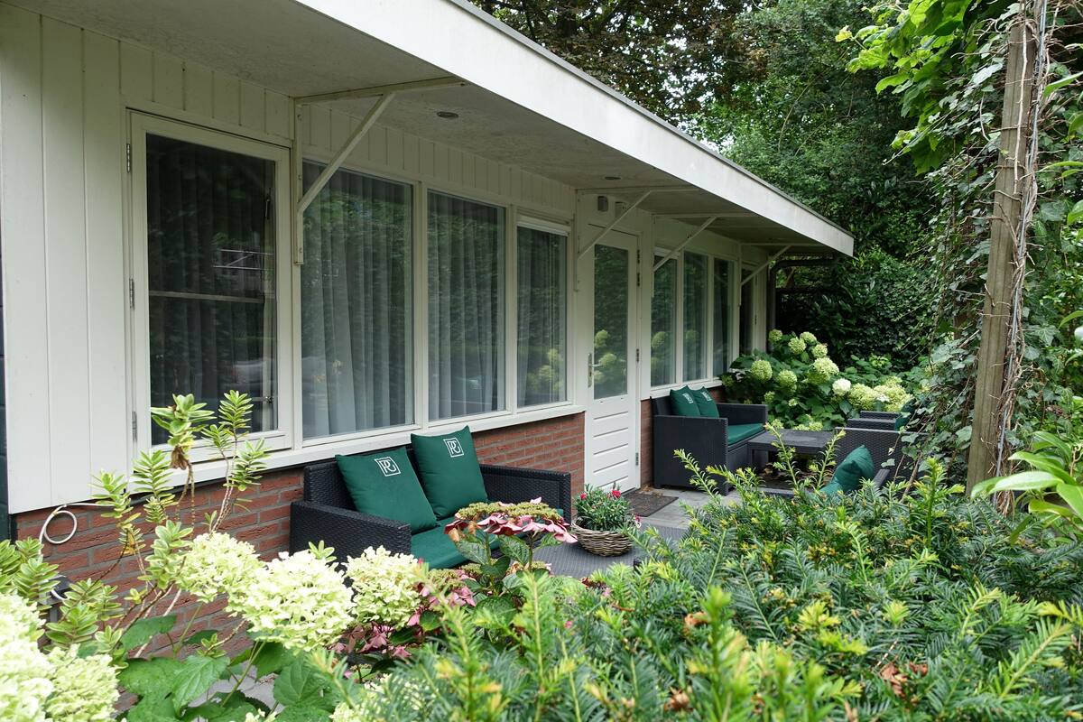 Un patio cubierto con mobiliario exterior, rodeado de exuberante follaje y plantas.