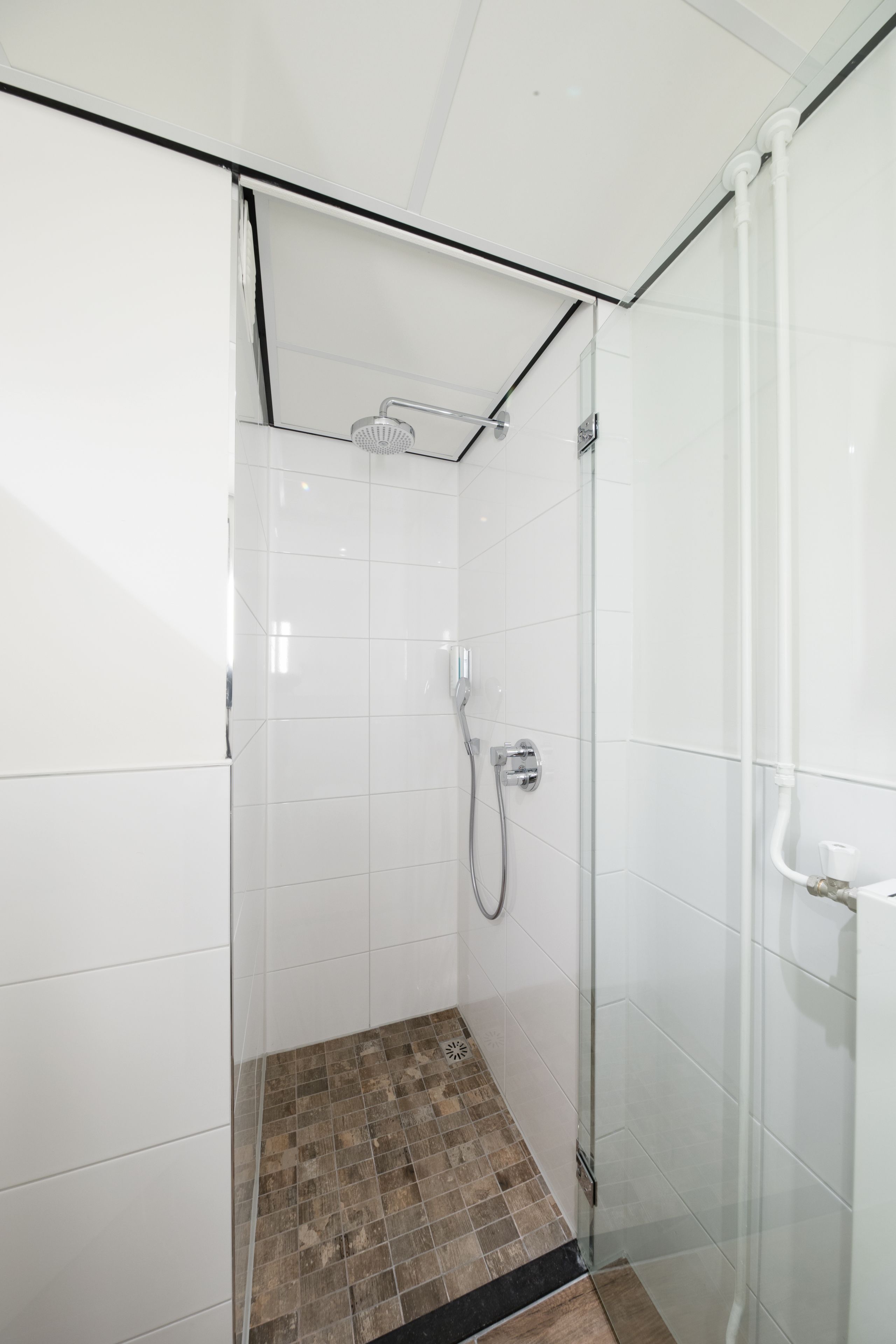 Un espace douche moderne doté d’une porte en verre, de murs recouverts de carreaux blancs et d’un pommeau de douche.