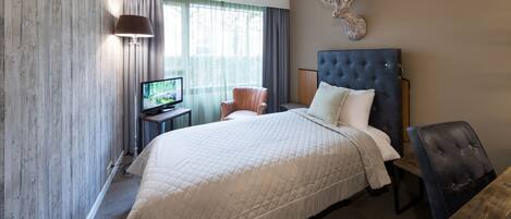 Una habitación de hotel con una cama grande, televisor, una silla y una cabeza de ciervo decorativa en la pared.