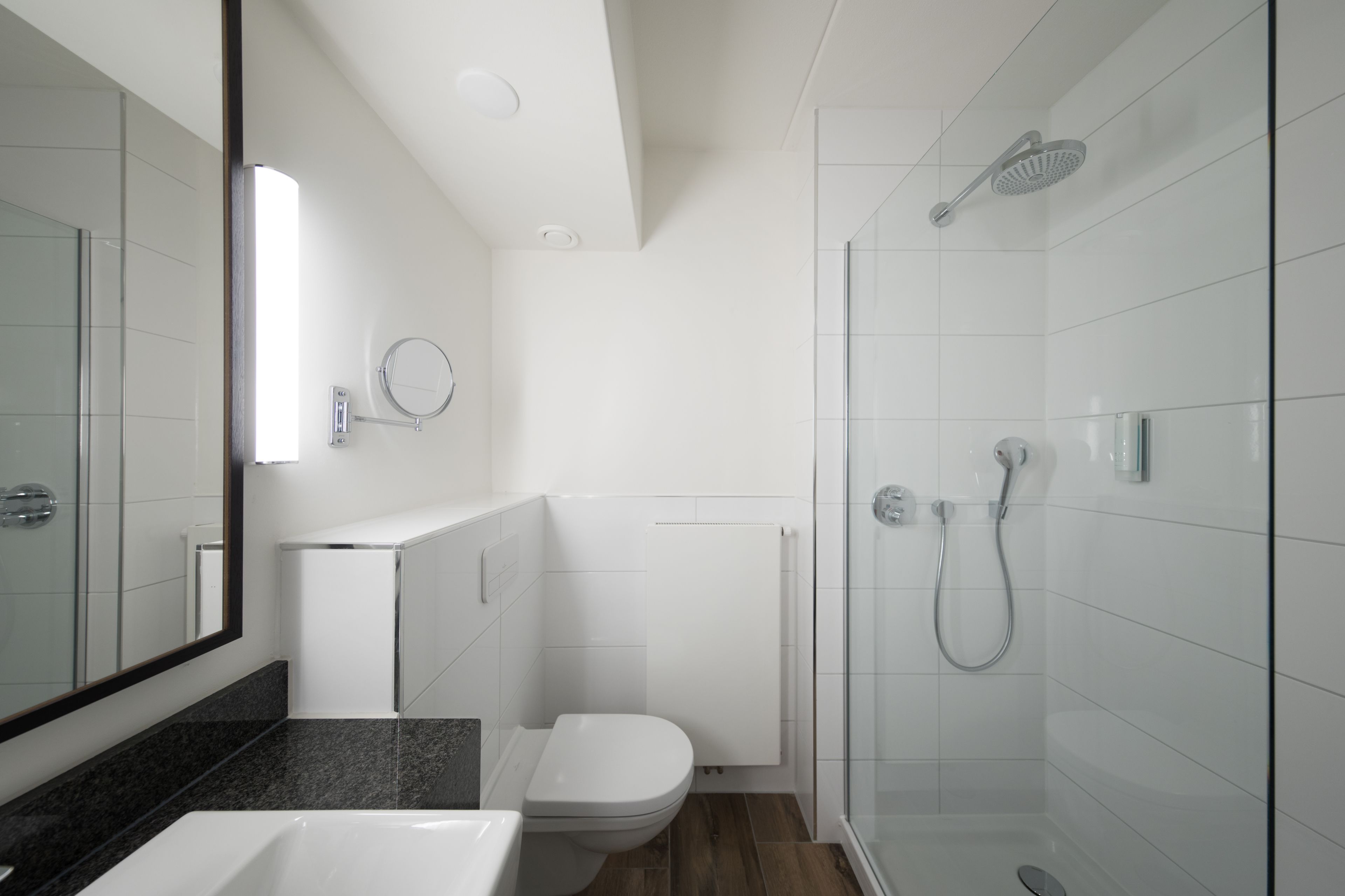 A modern bathroom with a glass shower enclosure, a white toilet, and a granite countertop.