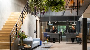 A modern lobby with a wooden staircase, seating area, reception desk, and hanging plants. - Bilderberg Hotel 't Speulderbos (Garderen)