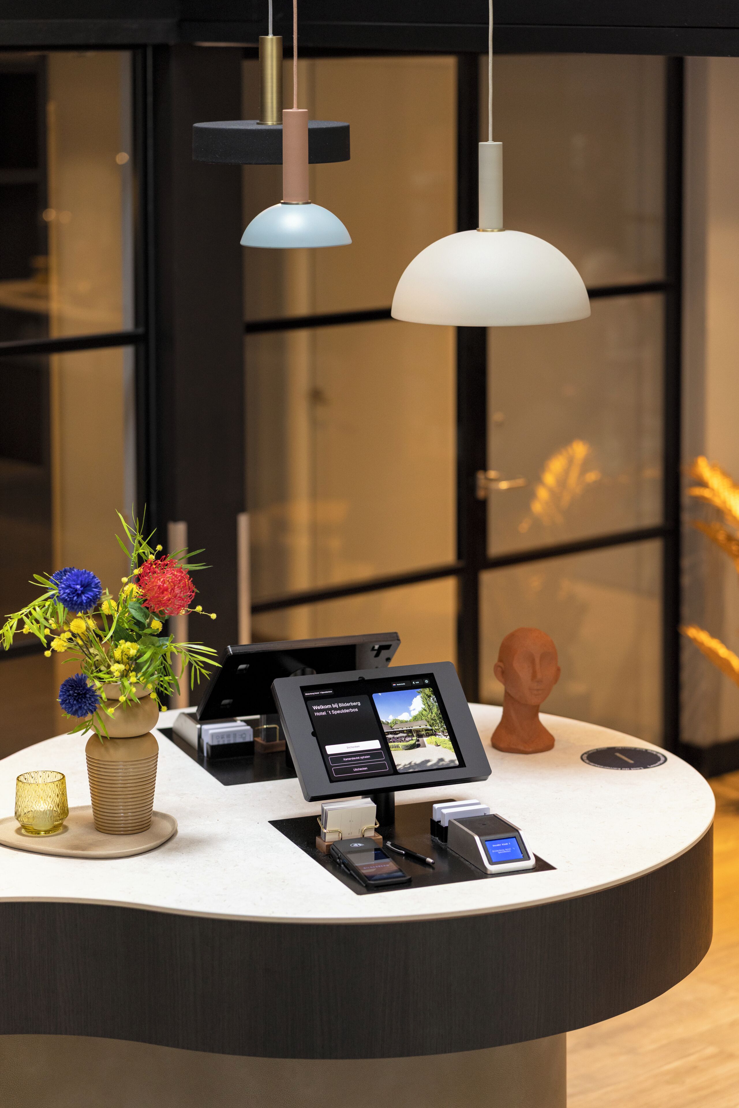 A reception desk with a digital display, a vase of flowers, and a bust sculpture.
