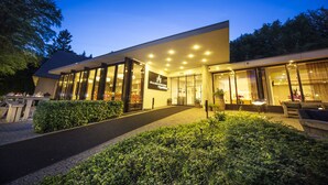 A modern building with large glass windows, a paved entrance, and a well-maintained garden area. - Bilderberg Hotel 't Speulderbos (Garderen)