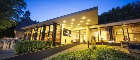 A modern building with large glass windows, a paved entrance, and a well-maintained garden area.