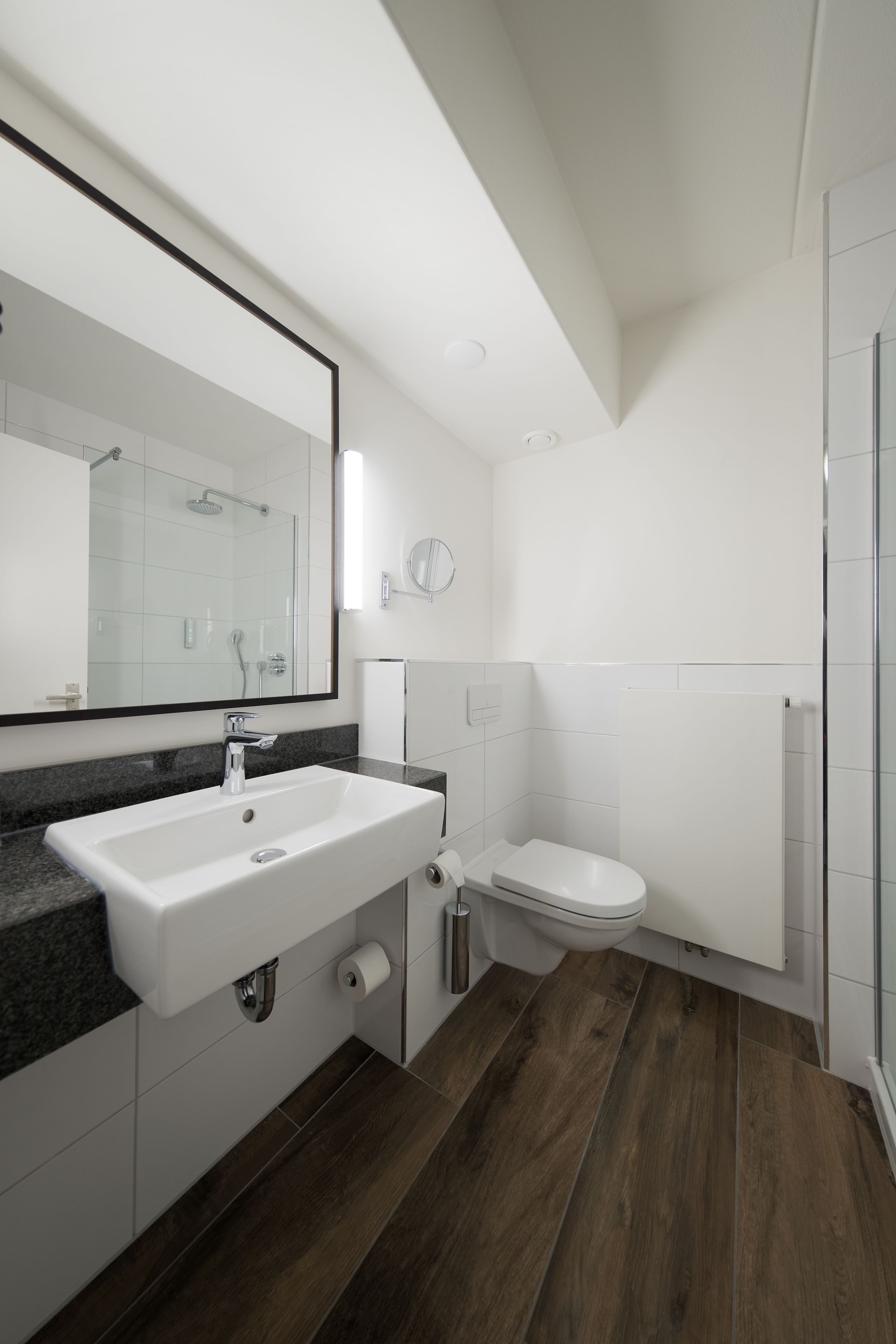 A modern bathroom with a white sink, mirror, and toilet.