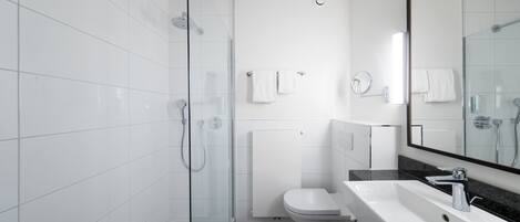 Un baño moderno con cabina de ducha de vidrio, inodoro blanco y lavamanos con espejo.