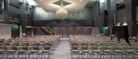 A conference room with rows of chairs, a chandelier, and a sign reading "TSPEULD".