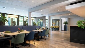 A modern restaurant with wooden flooring, blue and green seating, and potted plants. - Bilderberg Hotel 't Speulderbos (Garderen)