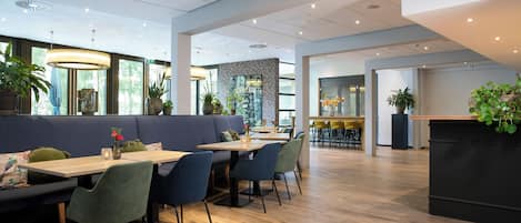 A modern restaurant with wooden flooring, blue and green seating, and potted plants.