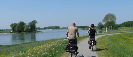 Two people riding bicycles on a paved path alongside a body of water.