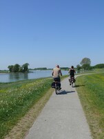 Dos personas andan en bicicleta por un camino pavimentado junto al agua.