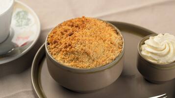 Un postre en un bol con cobertura desmenuzable, acompañado de un recipiente con crema batida.