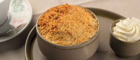 A dessert in a bowl with a crumbly topping, accompanied by a small container of whipped cream.