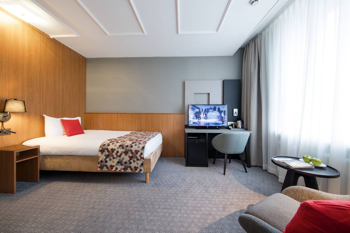 A hotel room with a bed, desk, chair, and a small table with fruit.