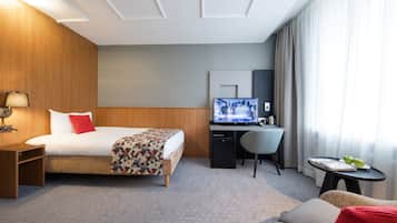 Habitación de hotel con cama, escritorio, silla y una pequeña mesa con fruta.