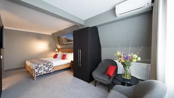 Una habitación de hotel moderna con una cama, un armario negro, un sillón gris, una pequeña mesa con un florero y un aire acondicionado instalado en la pared.