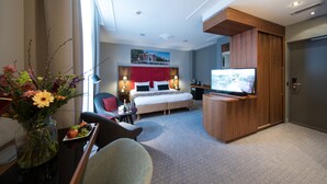 Habitación de hotel con cama, televisión, escritorio y un florero, además de una silla.