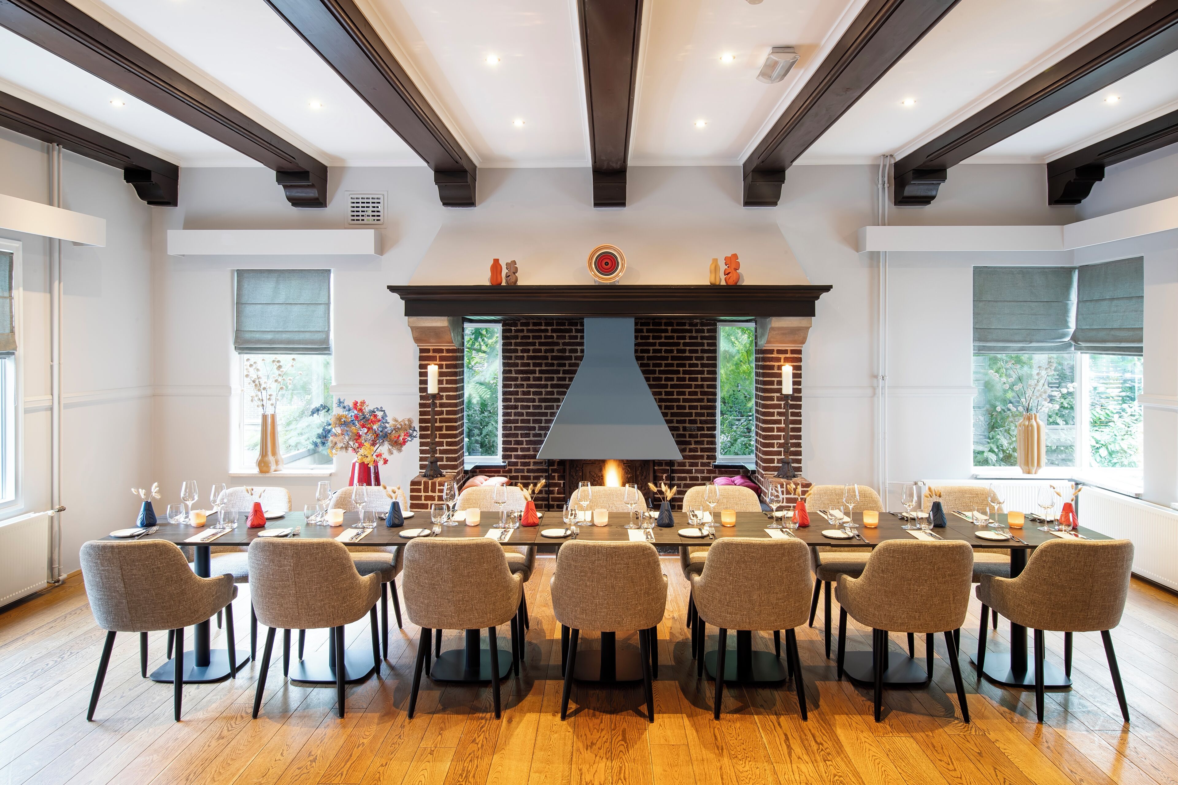 A dining area with a brick fireplace, wooden beams, and a long table set for eight.