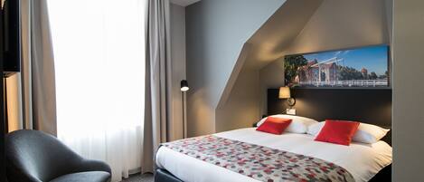 A hotel room with a large bed, a chair, a small table with apples, and a painting on the wall.