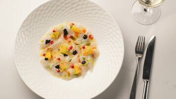 A white textured plate with a seafood dish, accompanied by a wine glass and cutlery on a white surface.