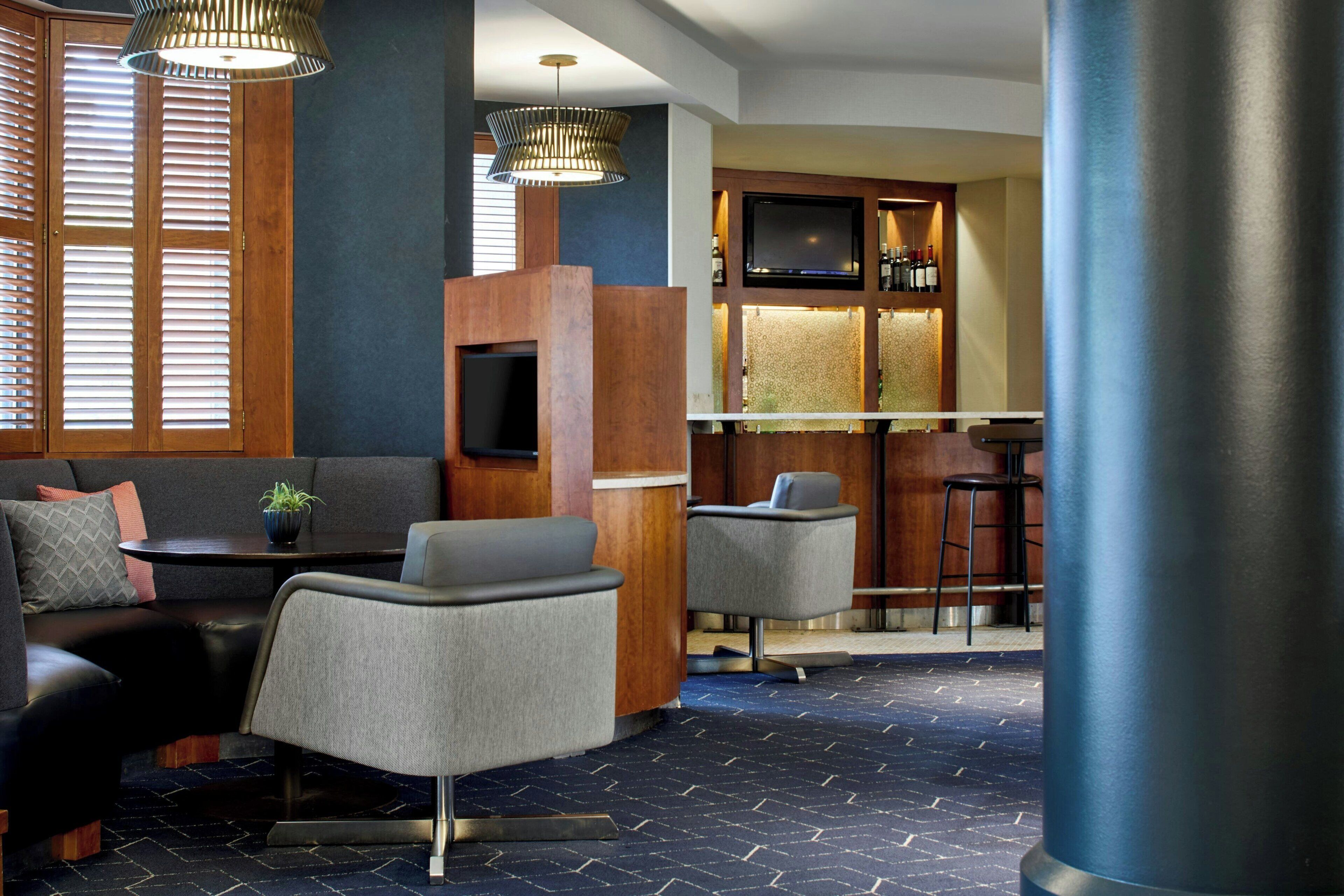 A modern lounge area with a sofa, armchairs, a small table, a TV, and a bar area with stools.
