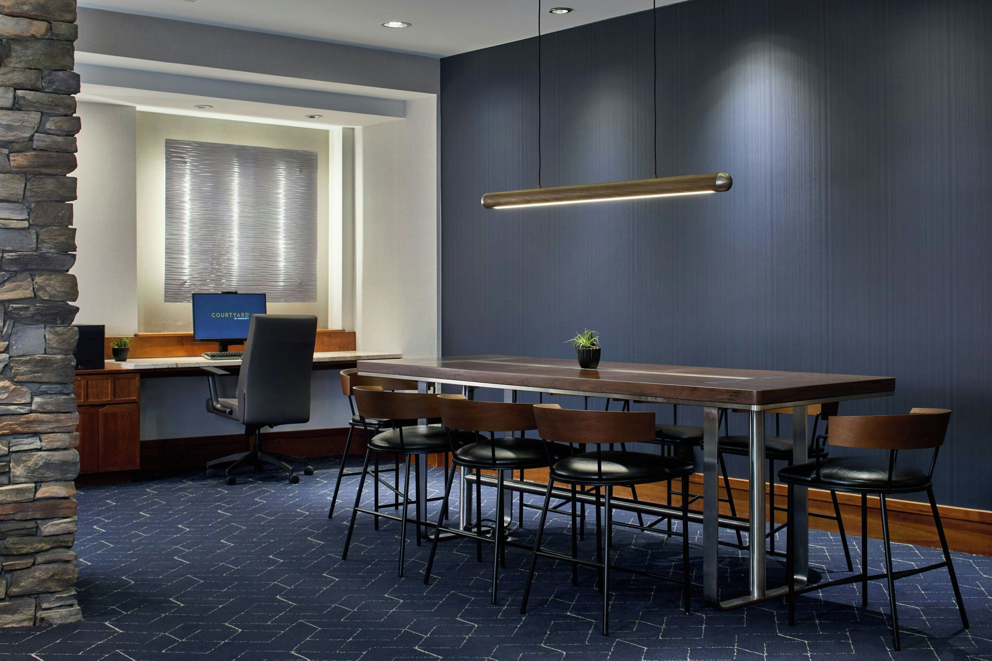 A conference room with a long table, chairs, a computer, and a window with blinds.