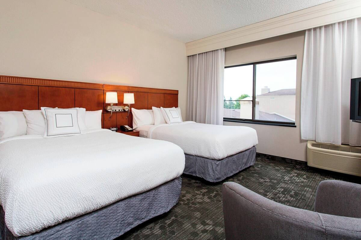 A hotel room with two beds, a TV, a desk, and a chair.