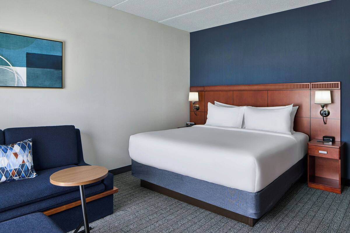 A hotel room with a bed, a sofa, a round table, and a painting on the wall.