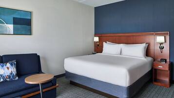 Quarto de hotel com uma cama, um sofá, uma mesa redonda e um quadro na parede.