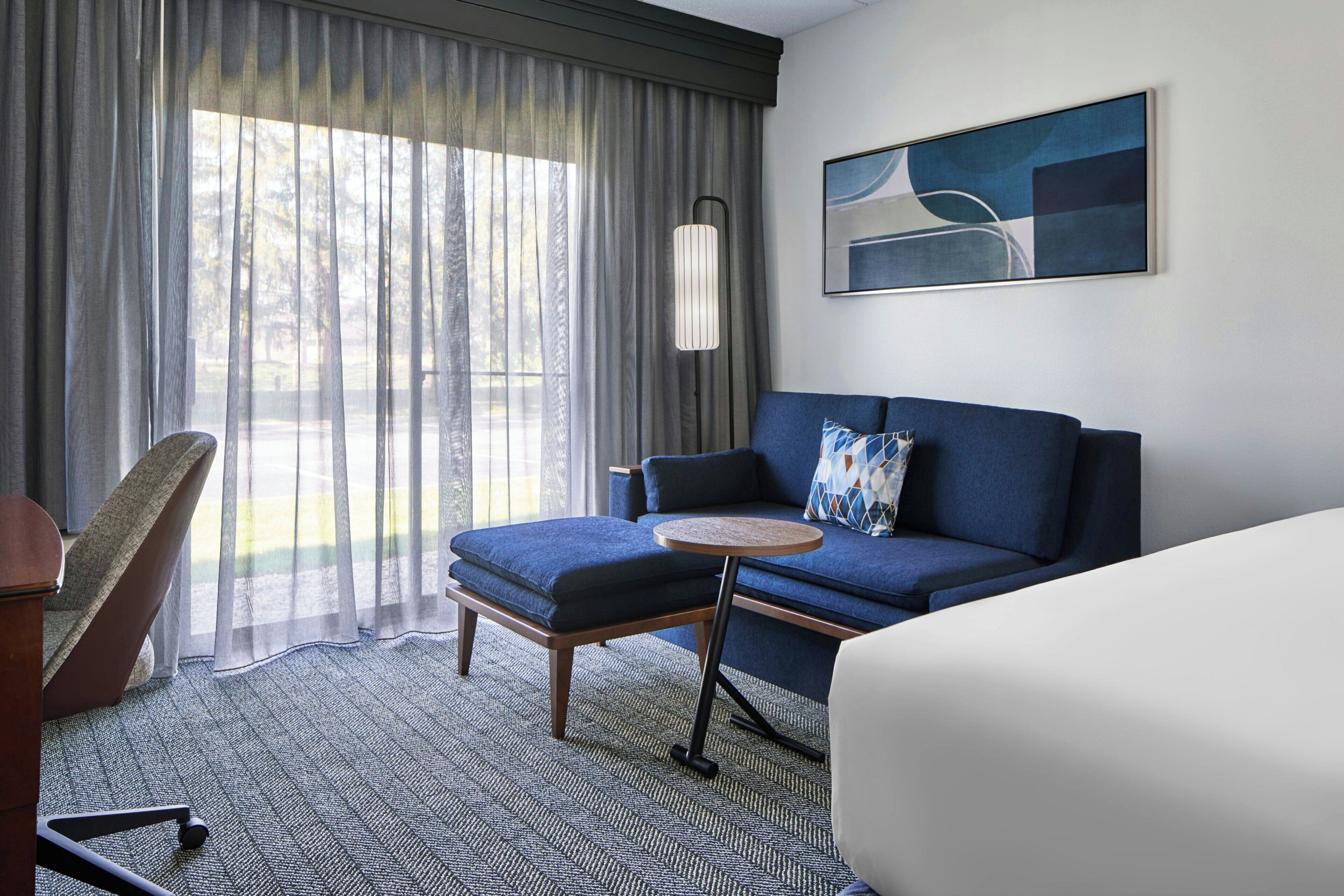 Une chambre d’hôtel avec un canapé, une petite table ronde, une chaise, un lit, une lampe et un tableau au mur.
