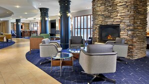 A lobby with a stone fireplace, seating area, and a large TV screen. - Courtyard by Marriott Rochester Brighton (Rochester)