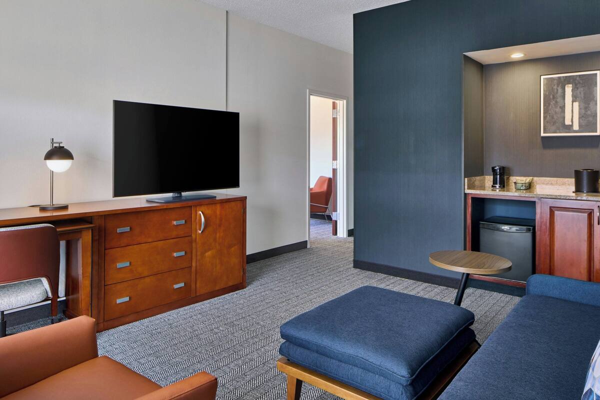 A modern hotel room with a flat-screen TV, wooden furniture, a small round table, and a sofa.