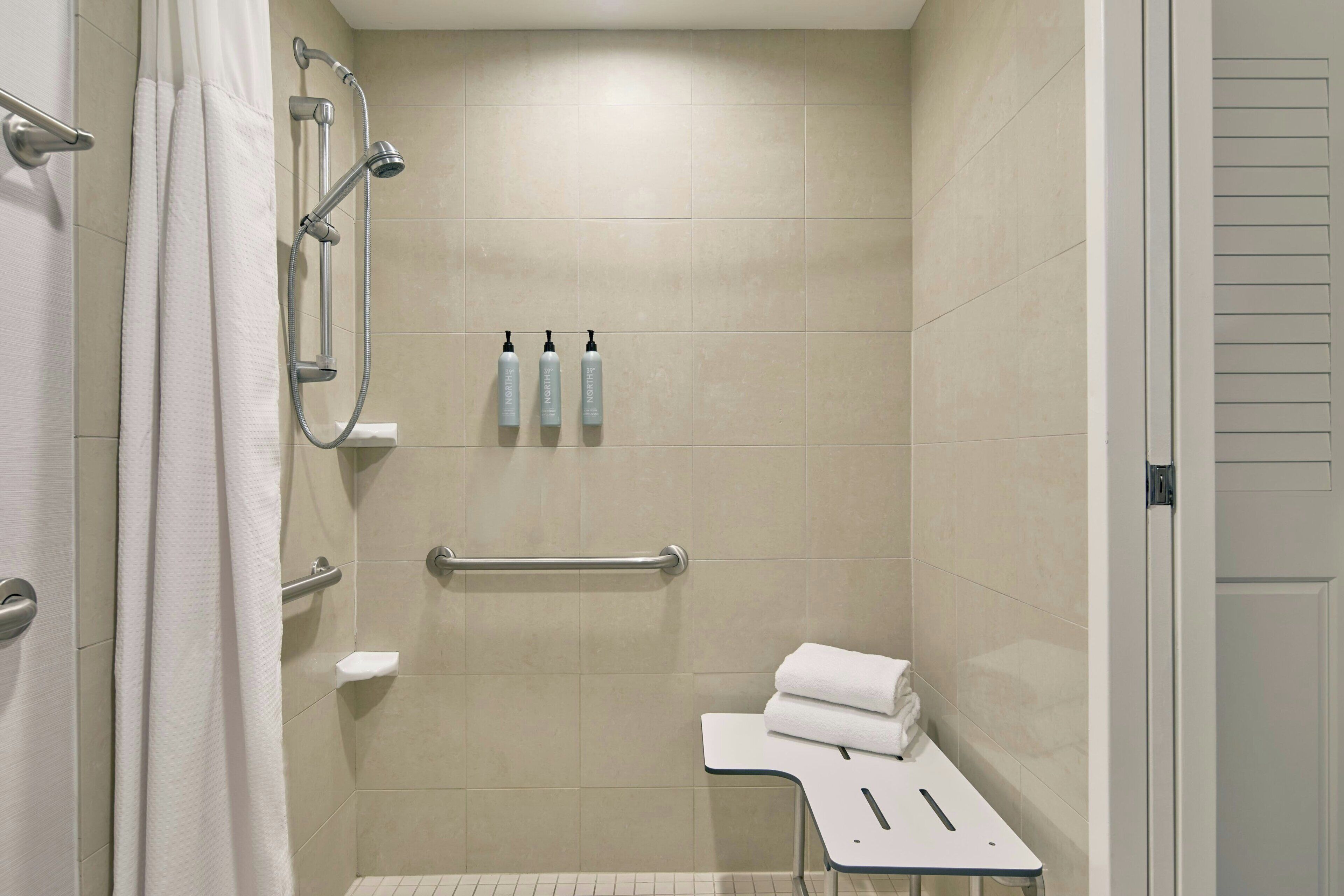A shower with a grab bar, a towel rack with bottles, and a small table with a towel.