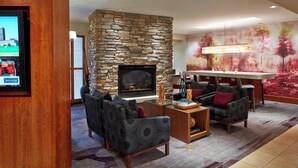 A modern living room with a stone fireplace, comfortable seating, a flat-screen TV, and a bar area. - Courtyard by Marriott Rochester Brighton (Rochester)
