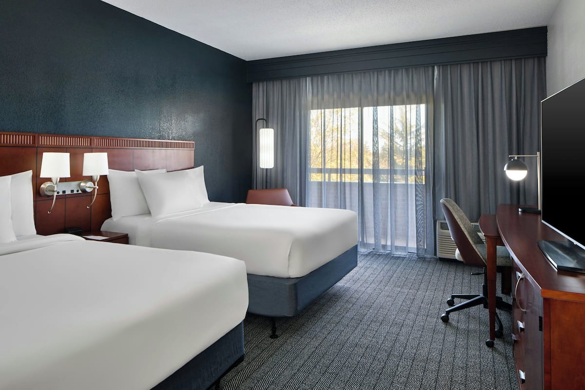 A hotel room with two beds, a desk, a chair, a TV, and a window with curtains.