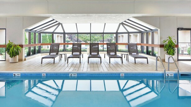 A swimming pool with lounge chairs, a glass ceiling, and potted plants. - Courtyard by Marriott Rochester Brighton (Rochester)