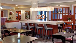 A restaurant with a central bar, multiple seating areas, and a view of the city through large windows. - Courtyard by Marriott Rochester Brighton (Rochester)