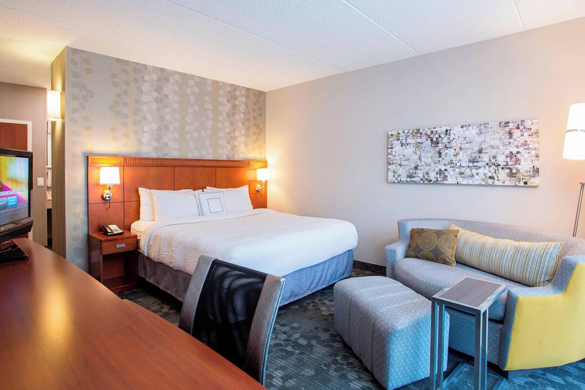 A hotel room with a bed, a desk, a chair, a sofa, and a small table.