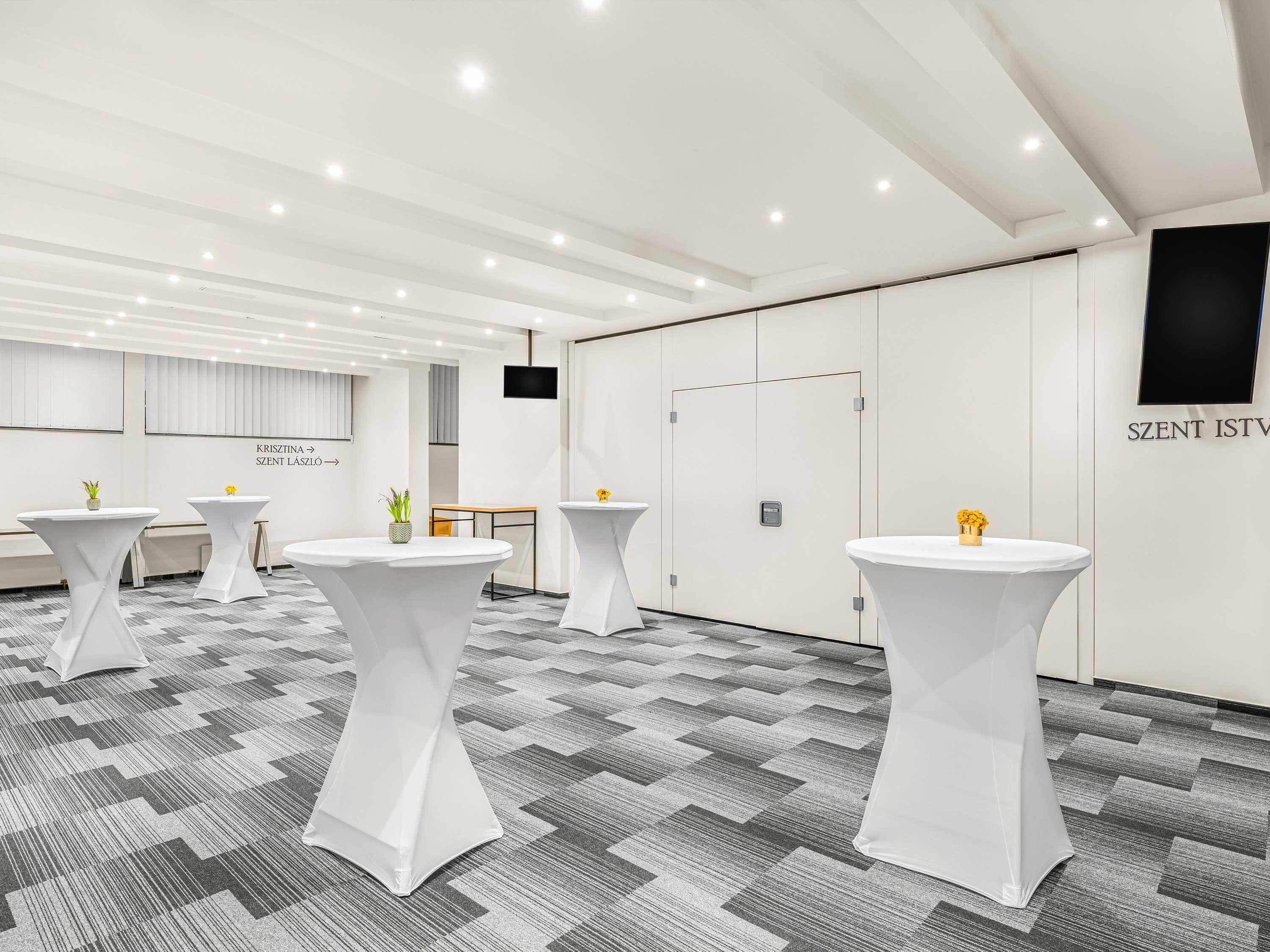 A conference room with white tables, grey patterned carpet, and a whiteboard with text.