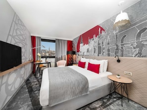 A hotel room with a bed, a desk, a TV, a window with curtains, and a cityscape mural.