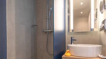 Un baño moderno con cabina de ducha de vidrio, lavamanos con espejo y toallas ordenadas.