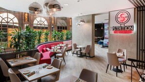 A modern restaurant interior with high ceilings, large windows, and a mix of seating arrangements including tables and a red booth. - Mercure Budapest Castle Hill (Budapest)