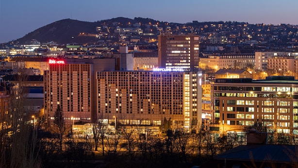A hotel with multiple floors, a prominent sign, and a view of the surrounding cityscape at dusk. - Mercure Budapest Castle Hill (Budapest)